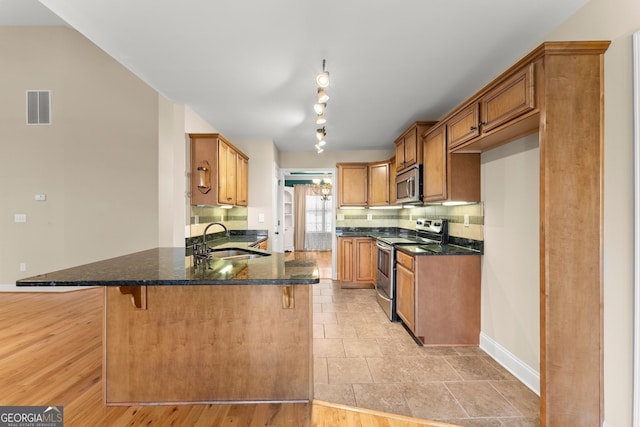 kitchen featuring visible vents, brown cabinetry, a breakfast bar, stainless steel appliances, and a sink