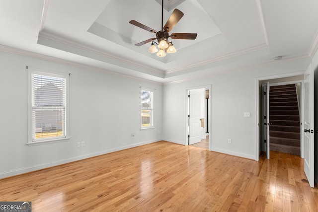 unfurnished bedroom with ceiling fan, light wood-style flooring, baseboards, a tray ceiling, and crown molding