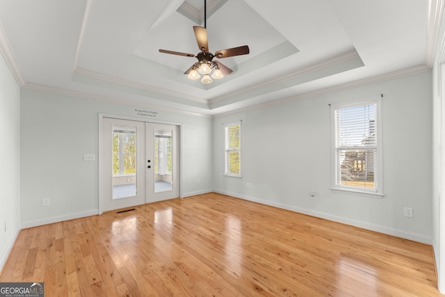 spare room with light wood-style floors, a wealth of natural light, a raised ceiling, and french doors