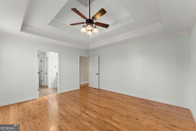 unfurnished bedroom featuring crown molding, light wood-type flooring, a raised ceiling, and baseboards