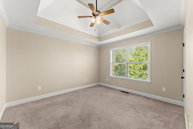 unfurnished room with a tray ceiling, crown molding, light colored carpet, visible vents, and baseboards