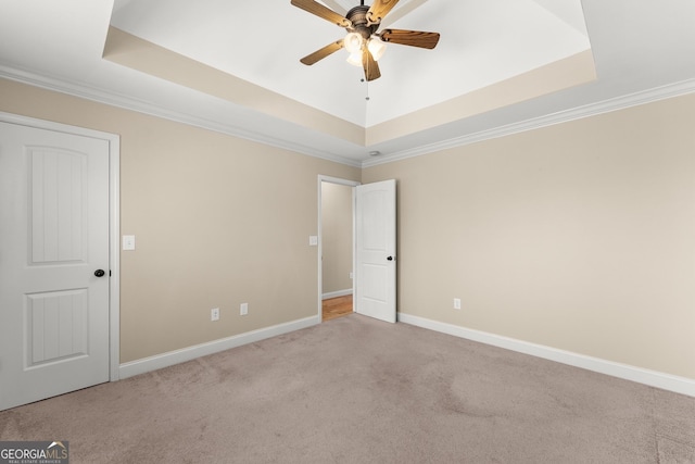 empty room with baseboards, a tray ceiling, ceiling fan, and light colored carpet