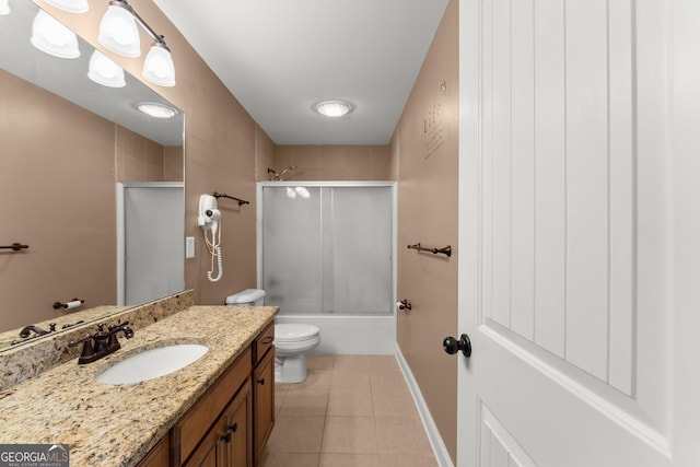 bathroom featuring bath / shower combo with glass door, toilet, vanity, baseboards, and tile patterned floors