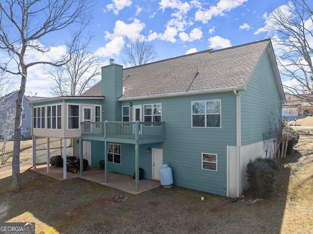 rear view of house with a patio area, a chimney, a sunroom, and roof with shingles