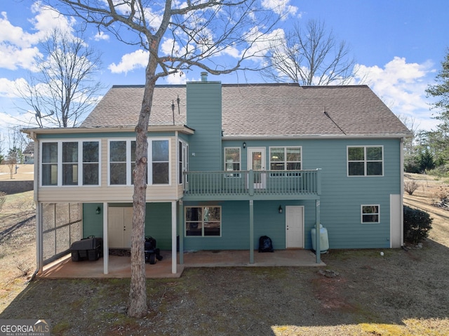 rear view of property with roof with shingles, a patio, a chimney, and a wooden deck