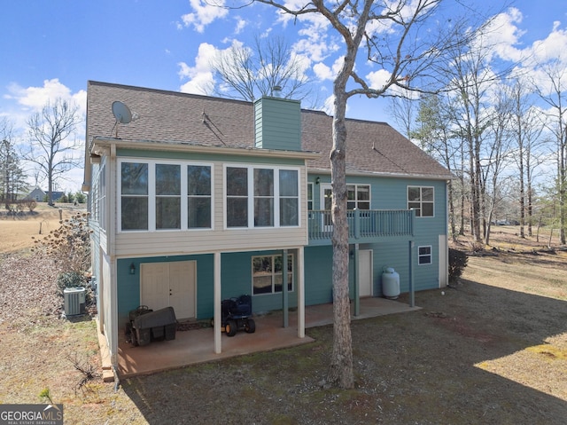 back of house featuring a shingled roof, cooling unit, a patio area, and a chimney