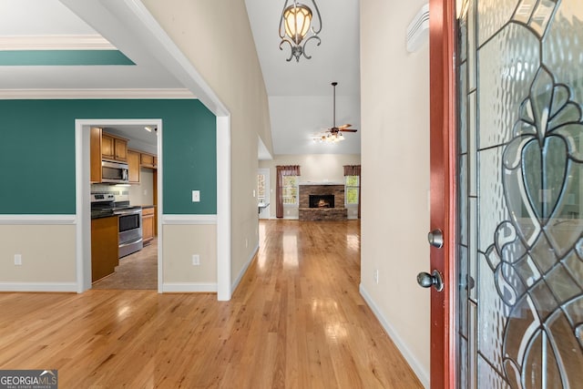 foyer featuring a warm lit fireplace, light wood-style flooring, crown molding, and ceiling fan with notable chandelier