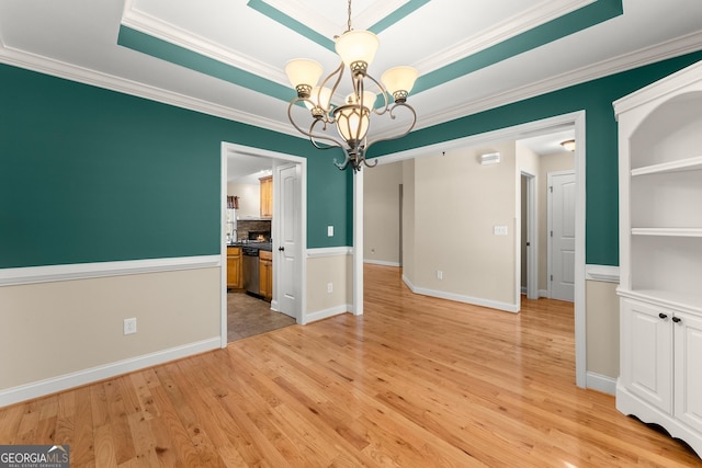 unfurnished dining area featuring light wood-style flooring, baseboards, an inviting chandelier, a raised ceiling, and crown molding