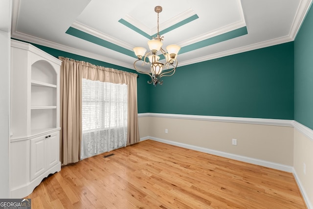 spare room featuring a tray ceiling, visible vents, a notable chandelier, and wood finished floors