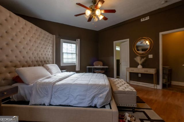 bedroom with a ceiling fan, visible vents, baseboards, and wood finished floors