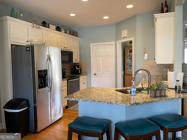 kitchen with a peninsula, appliances with stainless steel finishes, a sink, and light stone counters