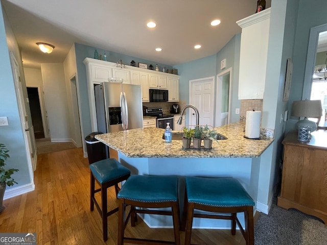 kitchen featuring black microwave, decorative backsplash, electric range oven, a peninsula, and white cabinetry