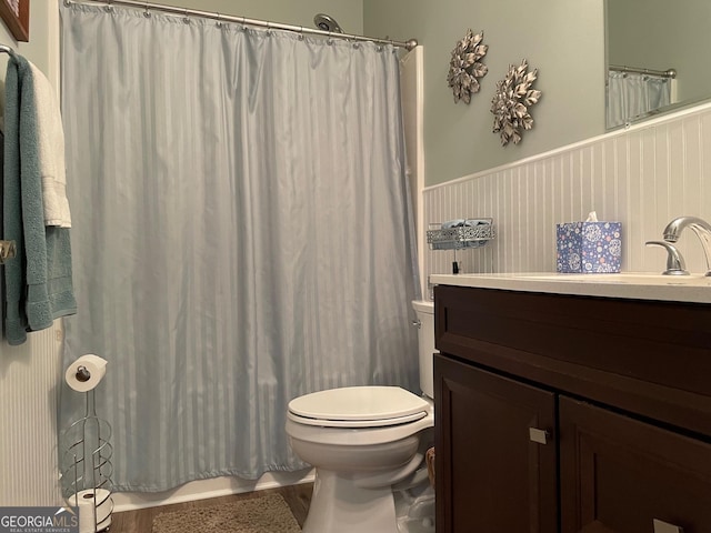 full bathroom featuring a shower with shower curtain, wainscoting, vanity, and toilet