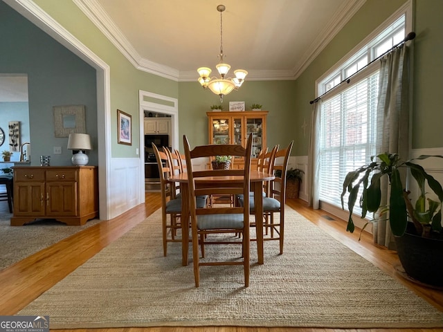 dining space featuring a decorative wall, a notable chandelier, light wood-style floors, wainscoting, and crown molding