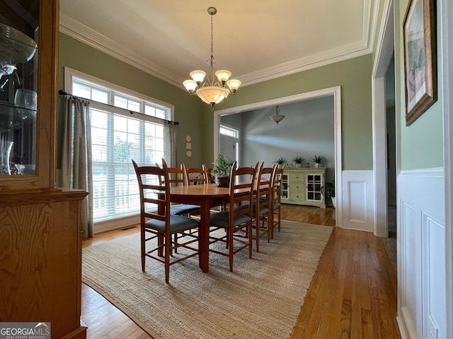 dining space with a wainscoted wall, ornamental molding, light wood finished floors, and an inviting chandelier