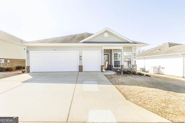 single story home with driveway, stone siding, an attached garage, and central AC