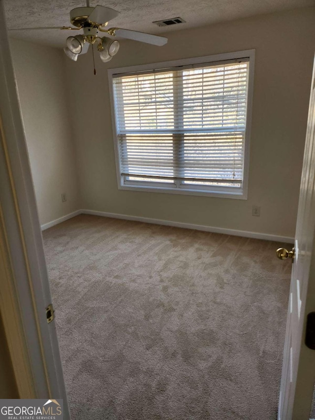 carpeted empty room featuring a healthy amount of sunlight, visible vents, ceiling fan, and a textured ceiling