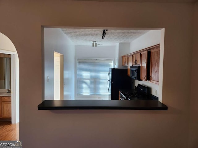 kitchen featuring dark countertops, a peninsula, rail lighting, a textured ceiling, and black appliances