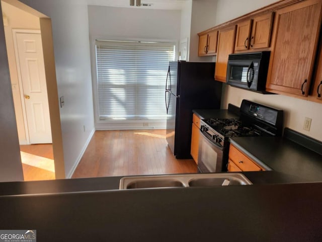 kitchen featuring dark countertops, brown cabinetry, black appliances, wood finished floors, and baseboards