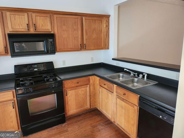 kitchen featuring dark countertops, a sink, black appliances, and wood finished floors