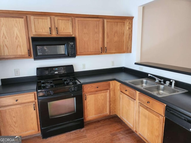 kitchen featuring dark countertops, black appliances, a sink, and wood finished floors