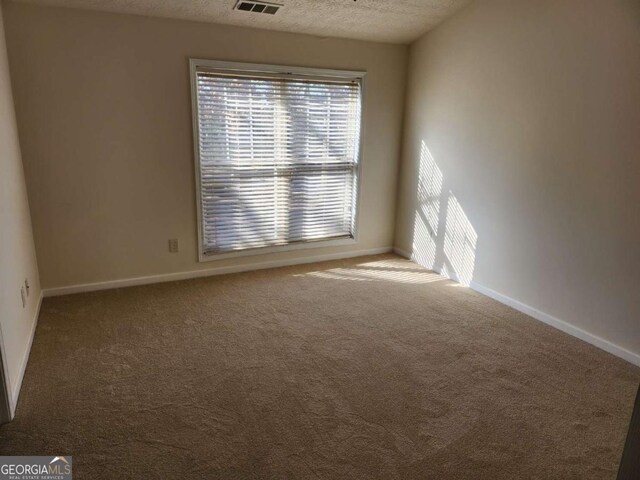 empty room with visible vents, carpet flooring, a textured ceiling, and baseboards