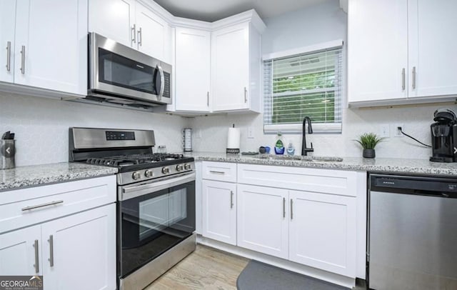 kitchen featuring appliances with stainless steel finishes, light stone counters, a sink, white cabinetry, and backsplash