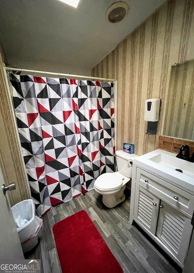 full bathroom with toilet, wallpapered walls, wood finished floors, and vanity