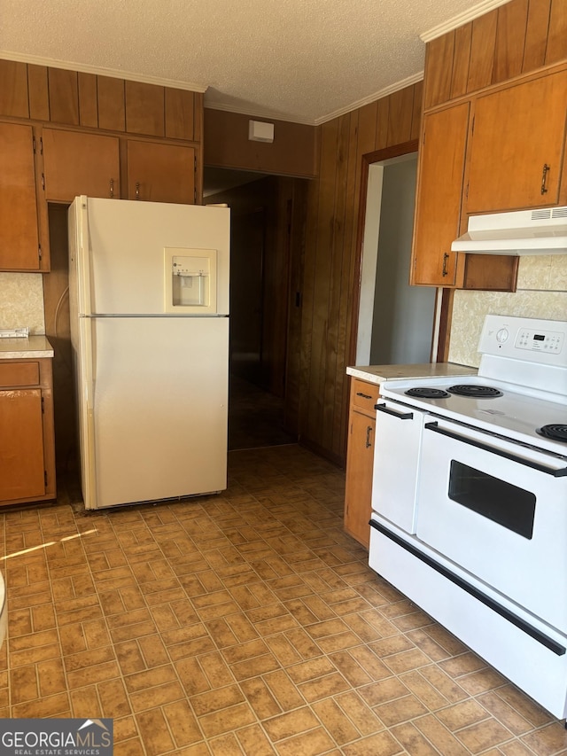 kitchen with wooden walls, under cabinet range hood, white appliances, light countertops, and brown cabinetry