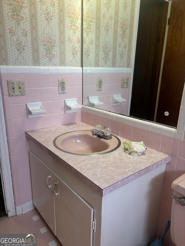 half bathroom featuring wallpapered walls, tile walls, a wainscoted wall, and vanity