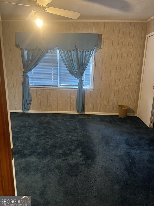 empty room featuring ornamental molding, dark carpet, wooden walls, and ceiling fan