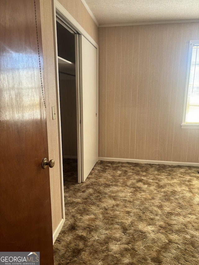 unfurnished bedroom with crown molding, a closet, dark colored carpet, and a textured ceiling