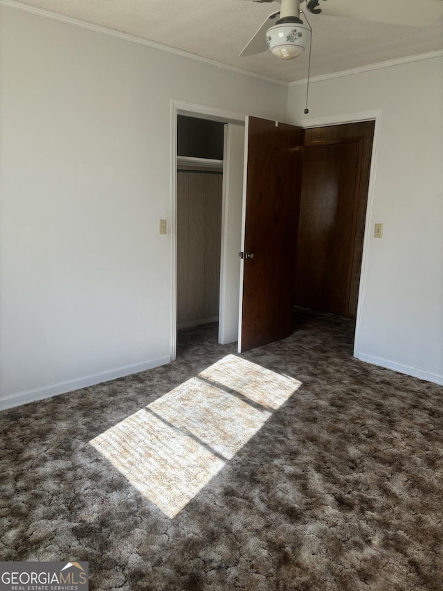 unfurnished bedroom with baseboards, ornamental molding, dark carpet, and a ceiling fan