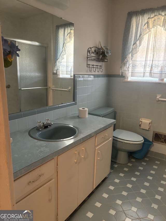 bathroom with a shower with door, tile walls, toilet, wainscoting, and vanity