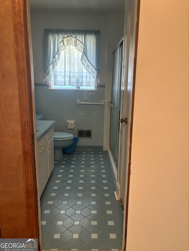 bathroom with a stall shower, toilet, tile patterned flooring, vanity, and tile walls