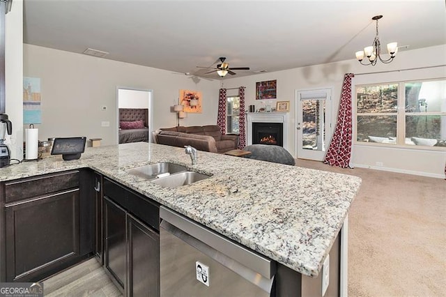 kitchen featuring light stone counters, a sink, open floor plan, a lit fireplace, and dishwasher