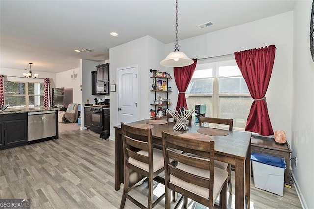 dining room with a healthy amount of sunlight, visible vents, light wood finished floors, and an inviting chandelier