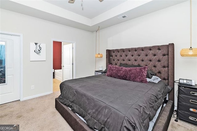 bedroom featuring a tray ceiling, light colored carpet, visible vents, ensuite bath, and baseboards