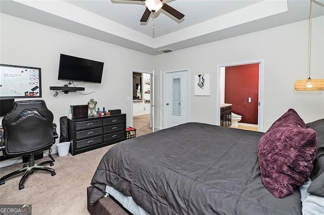 carpeted bedroom with ceiling fan, ensuite bath, visible vents, and a raised ceiling
