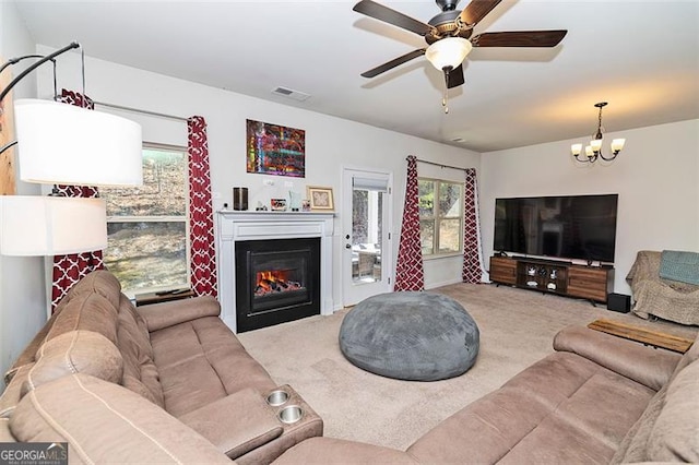 carpeted living room with ceiling fan with notable chandelier, a glass covered fireplace, and visible vents