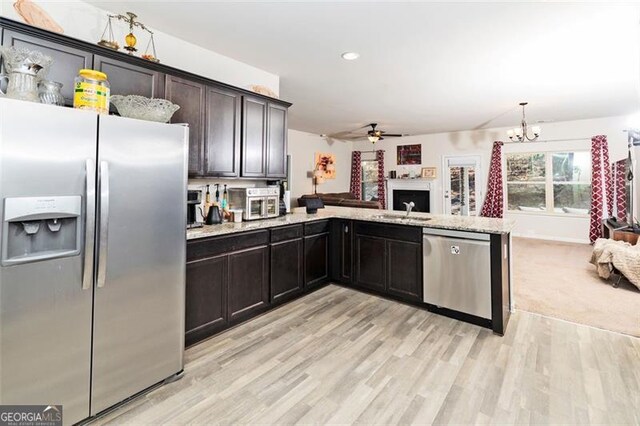 kitchen featuring open floor plan, stainless steel appliances, hanging light fixtures, and light wood finished floors