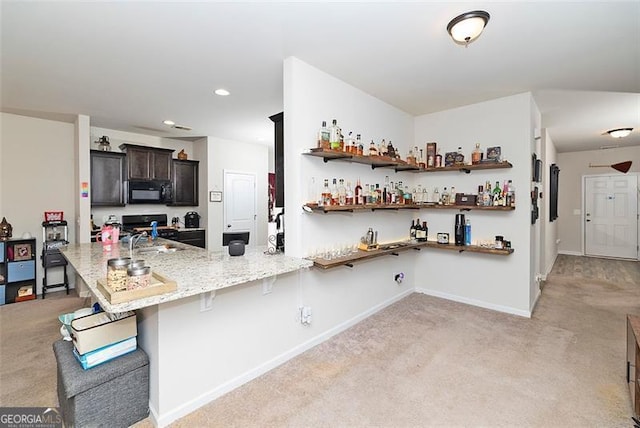 kitchen featuring black microwave, a peninsula, light carpet, and baseboards