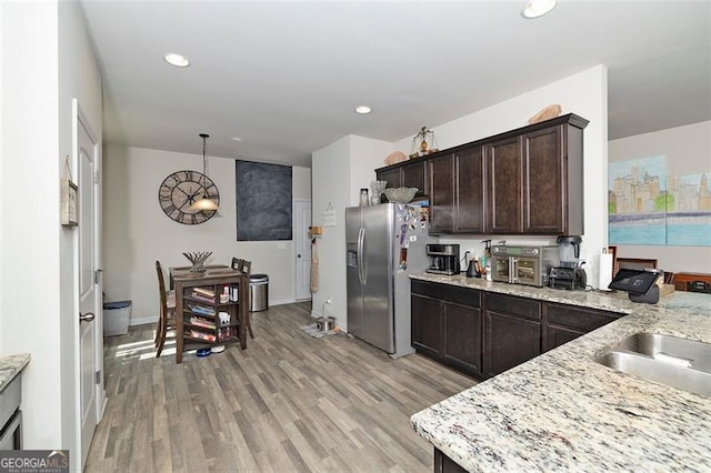 kitchen with dark brown cabinetry, stainless steel fridge, light wood-style flooring, hanging light fixtures, and light stone countertops