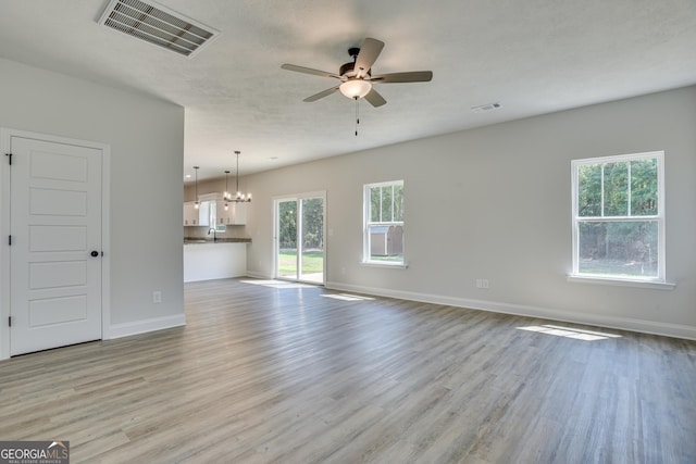 unfurnished living room with baseboards, visible vents, light wood finished floors, and ceiling fan with notable chandelier