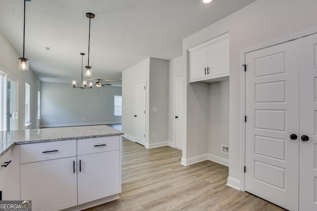 kitchen featuring light stone countertops, white cabinetry, pendant lighting, and open floor plan