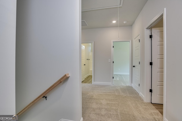 hallway featuring light colored carpet, visible vents, attic access, an upstairs landing, and baseboards