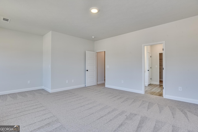 unfurnished room with visible vents, light carpet, and baseboards