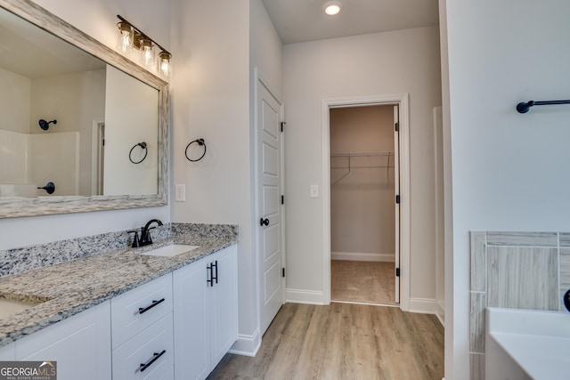 bathroom with a shower, a spacious closet, a sink, wood finished floors, and baseboards