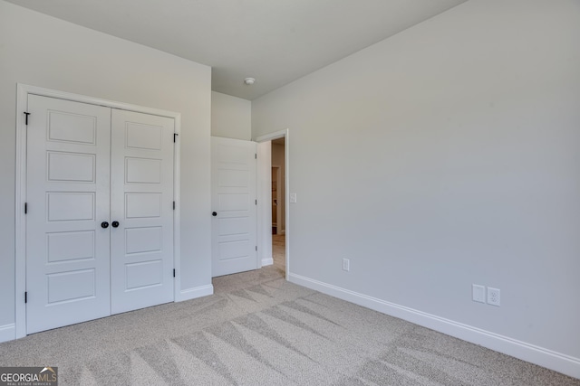 unfurnished bedroom with a closet, light colored carpet, and baseboards