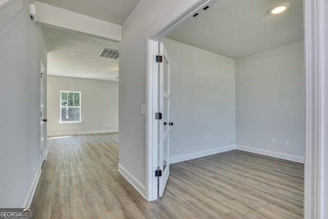 corridor featuring light wood-style flooring, visible vents, and baseboards